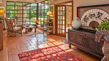 A spacious living room with a large window, a traditional Asian-style cabinet, and a red patterned rug.