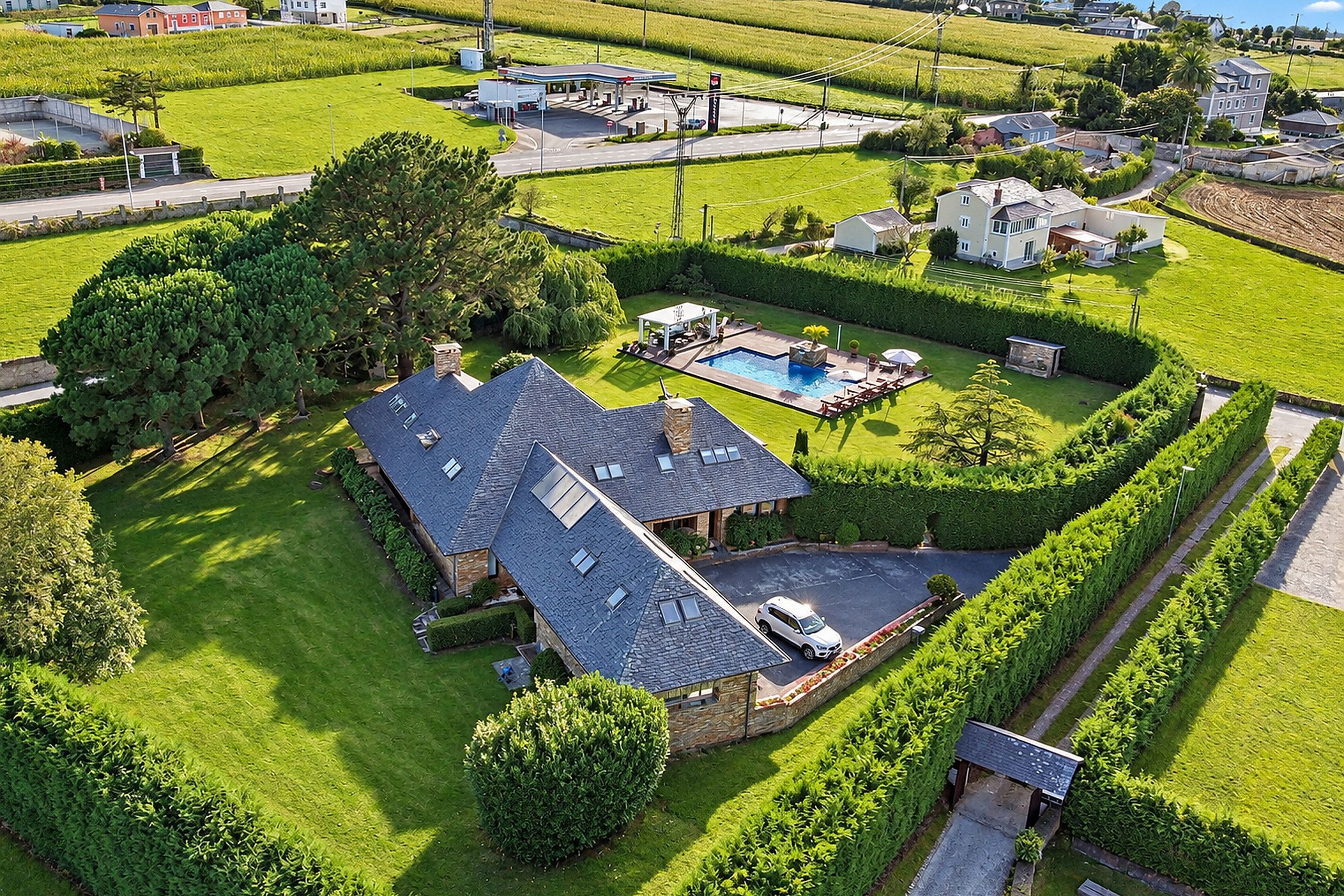 A residential property with a swimming pool, a well-maintained lawn, and a large house with a sloped roof.