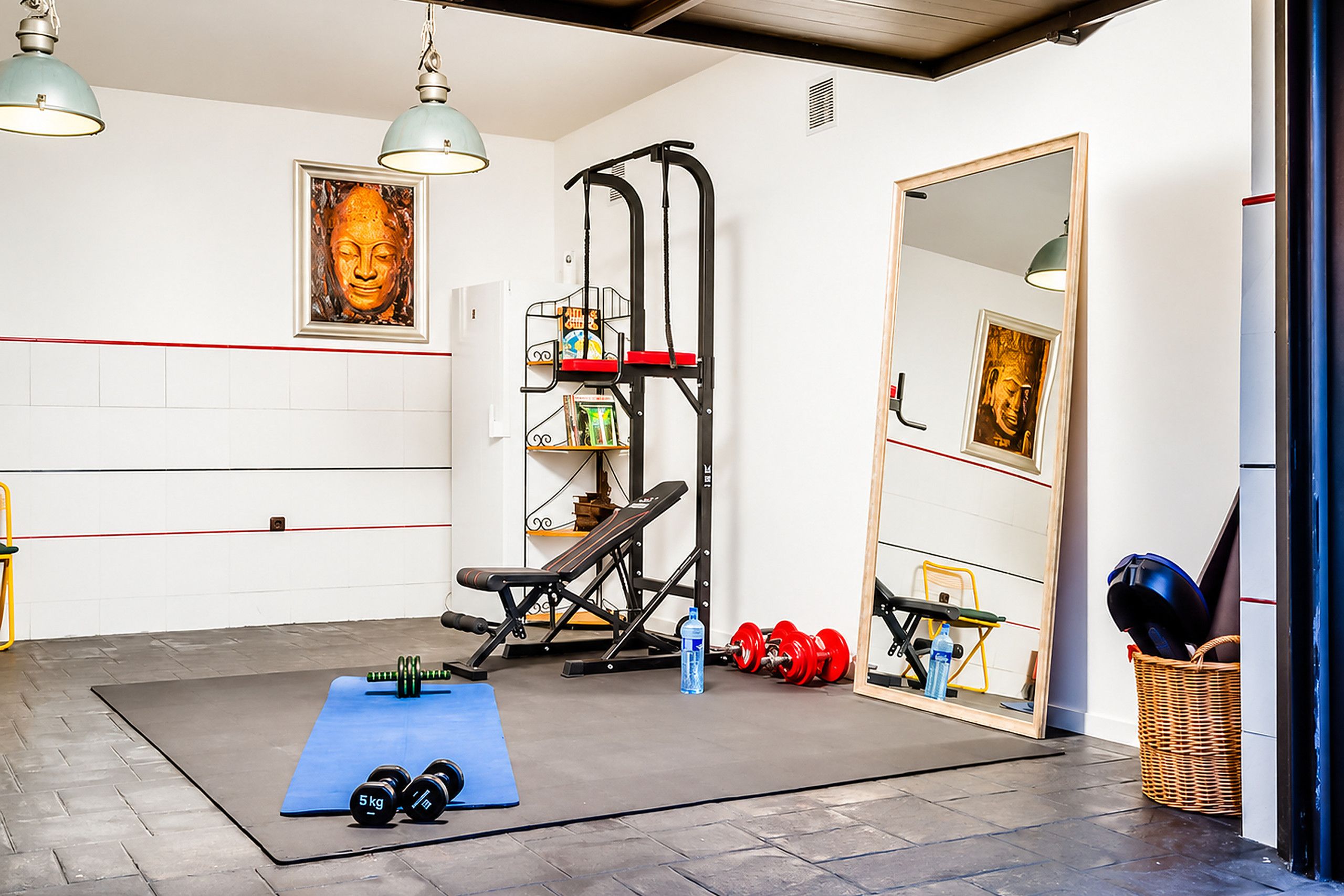 Une salle de sport équipée de matériel d’exercice, avec un tapis bleu, des haltères et un miroir.
