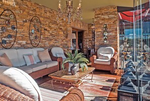 Una sala de estar amoblada con muebles de mimbre, pared de piedra y vista a través de un ventanal.