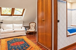 Una habitación con un sofá blanco, una alfombra estampada, un armario de madera y una esquina con bañera.