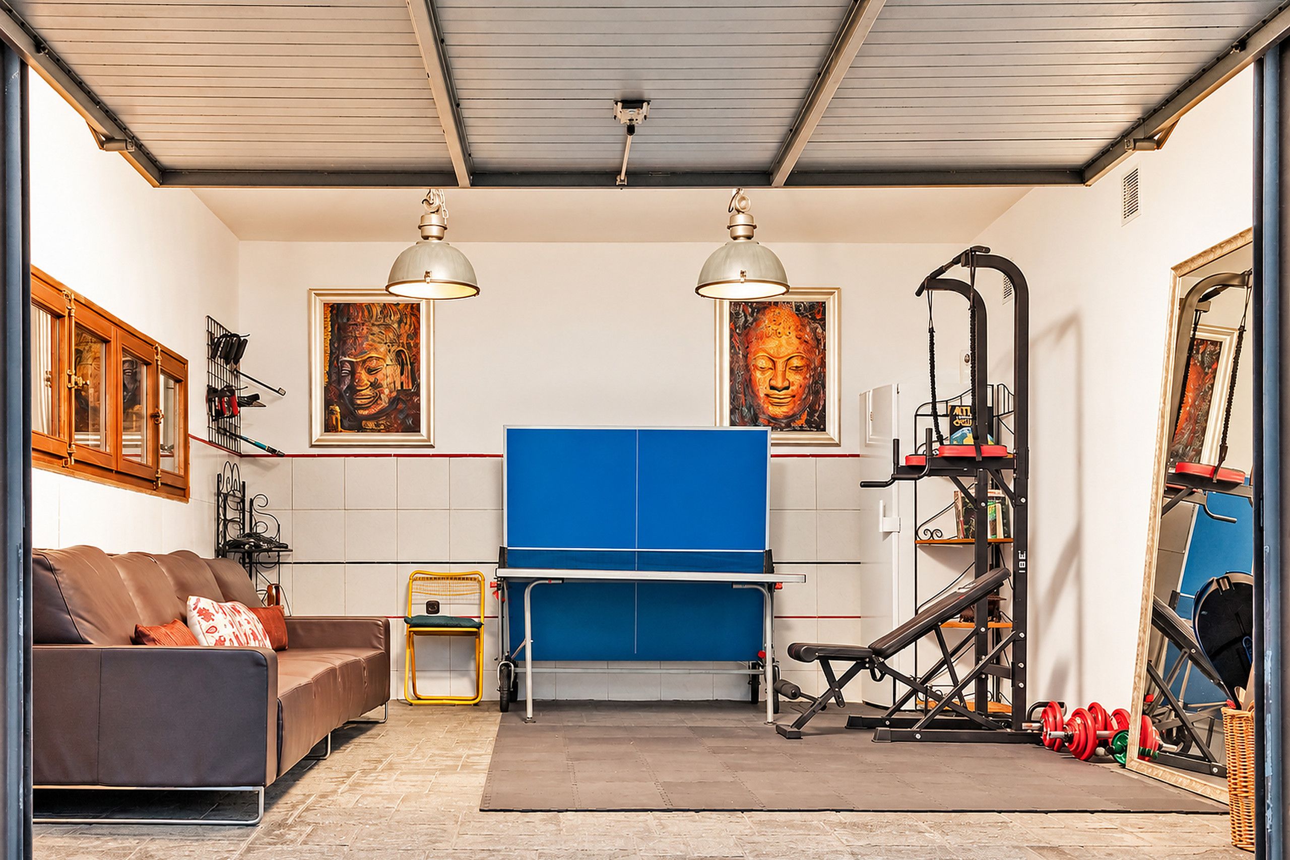 A compact living space with a sofa, a blue folding table, a bicycle, and a wall-mounted exercise machine.