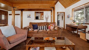 A cozy living room with a wooden ceiling, a brown sofa, a glass coffee table, and a desk with a lamp. - Resting Falcon#2661 (Big Bear City)