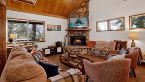 A cozy living room with a stone fireplace, wooden ceiling, and a mounted deer head. - Resting Falcon#2661 (Big Bear City)