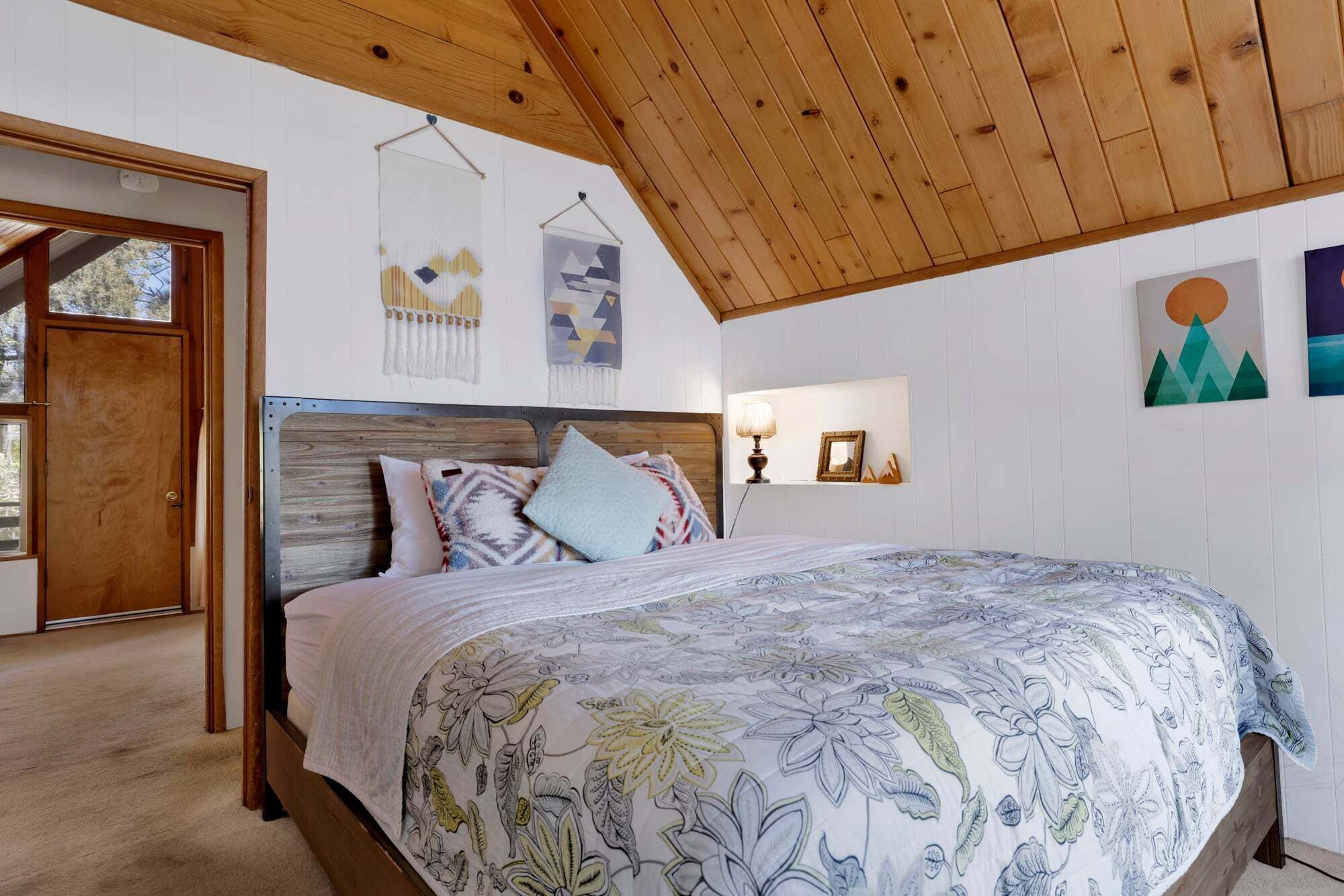 Een slaapkamer met een houten plafond, een bed met een bloemenbedekking, een houten hoofdbord en wanddecoratie.