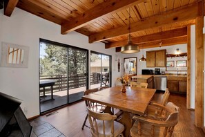 Un comedor amplio con una mesa y sillas de madera, una cocina con armarios de madera, y un amplio ventanal corredero que da a una terraza exterior.