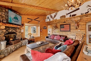 A rustic cabin interior with a stone fireplace, wooden walls, a leather sofa, and a mounted American flag.