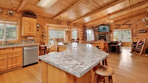 A rustic cabin with wooden walls, a stone fireplace, a kitchen with granite countertops, and a dining area with wooden chairs. - Aspen Bear Retreat#2610 (Big Bear City)