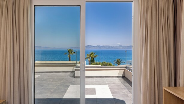 Una habitación con puerta de vidrio corrediza que da a un balcón con vistas al mar y a las montañas.