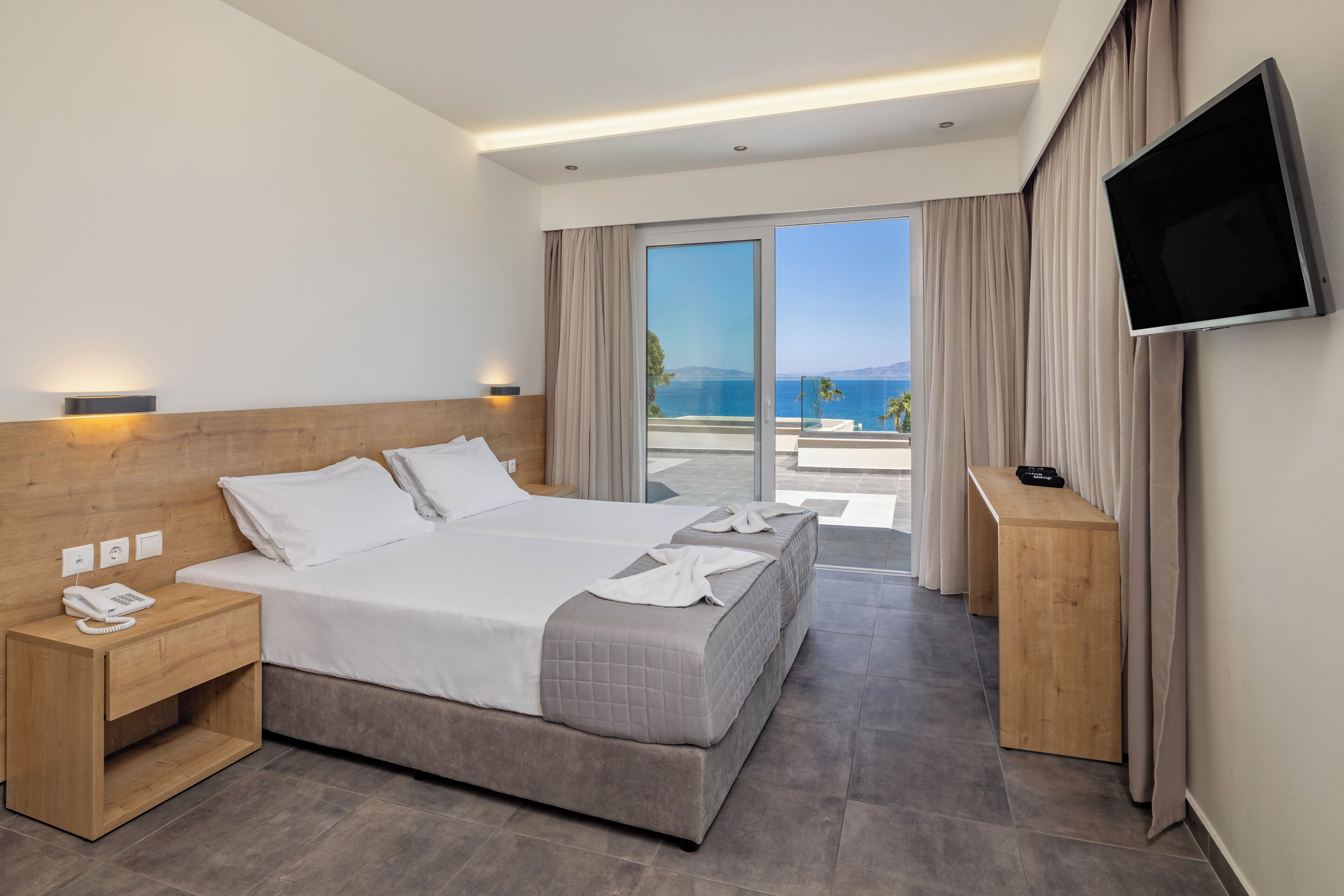 Habitación de hotel con una cama, televisión, mesita de noche y vistas al mar.