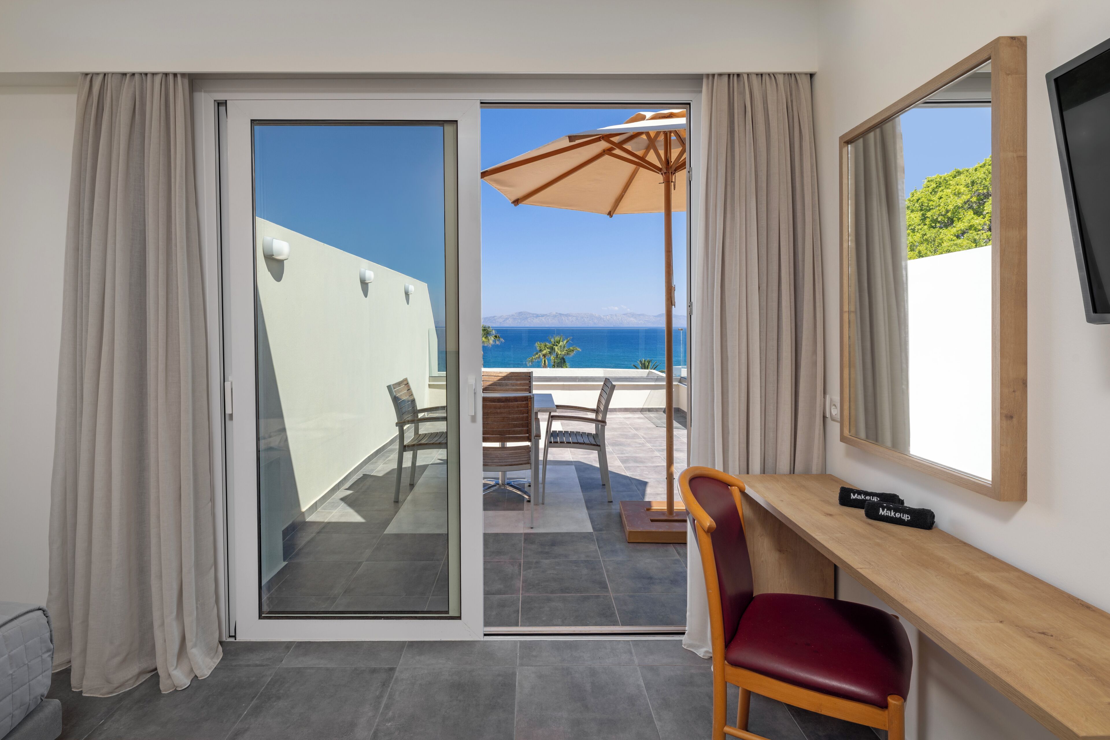 A room with a sliding glass door leading to a balcony with a table, chairs, and an umbrella.