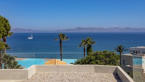 Vista costera con cielo despejado, piscina, palmeras y montañas a lo lejos.