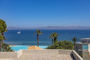 A coastal view with a clear sky, a swimming pool, palm trees, and distant mountains. - POSEIDONIA APARTMENTS (Ialisos)
