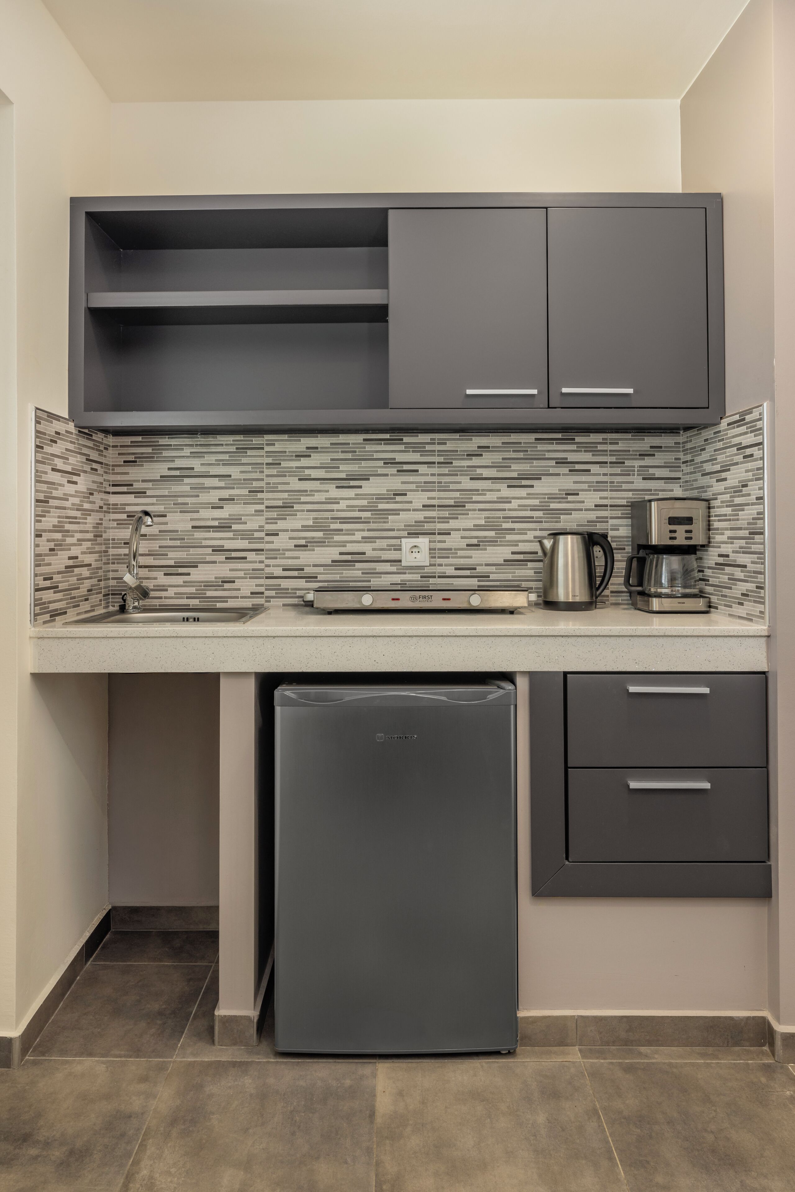 A compact kitchen with a built-in refrigerator, a coffee maker, and a microwave.