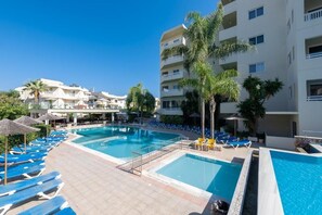 Zona de piscina con varias piscinas, sillas de descanso y palmeras.