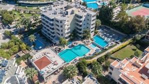 Un hotel de varios pisos con piscina en la azotea, cancha de tenis y un jardín ajardinado.