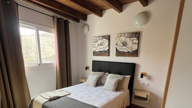 Una camera da letto con un letto, travi in legno, una finestra e opere d'arte alle pareti.
