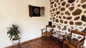 Una stanza con parete in pietra, un bersaglio da freccette, due sedie di legno, una pianta in vaso e pavimento piastrellato.