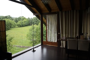A room with a large window, a wooden ceiling, and a dining area with chairs.