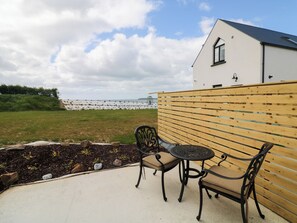 A patio with two chairs and a table, a wooden fence, and a building with a window. - Radharc an Hook @ Estuary Bliss (Duncannon)