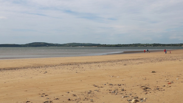 Een strand met een heldere lucht, kalm water en heuvels in de verte.