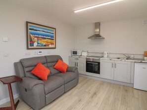 A compact living space with a sofa, kitchen area, and a painting on the wall. - Radharc an Hook @ Estuary Bliss (Duncannon)