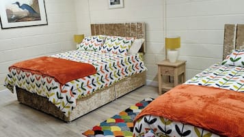 A room with two beds, a colorful rug, and a small table with a lamp.