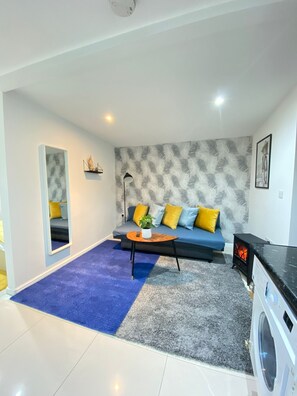 A modern living room with a sofa, a coffee table, a washing machine, and a patterned wall. - Tower Bridge Cozy Studio Up To 4 People (London)