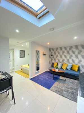 A modern living room with a skylight, a sofa with cushions, a coffee table, and a dining area with a table and chairs. - Tower Bridge Cozy Studio Up To 4 People (London)