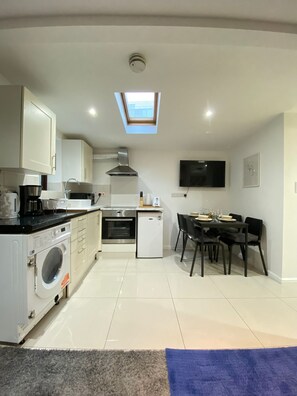 A compact kitchen with a built-in oven, microwave, and washing machine, a dining area with a table and chairs, and a TV mounted on the wall. - Tower Bridge Cozy Studio Up To 4 People (London)