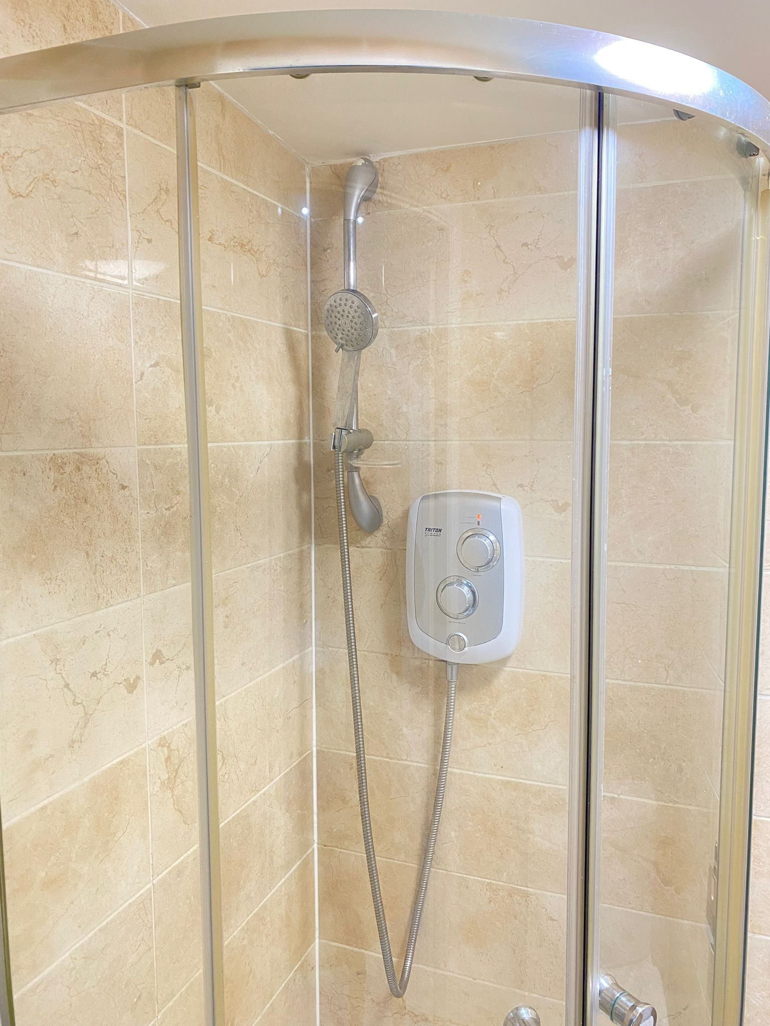 Eine begehbare Dusche mit Glaswänden, einer Handbrause und einer fest installierten Bedienkonsole.
