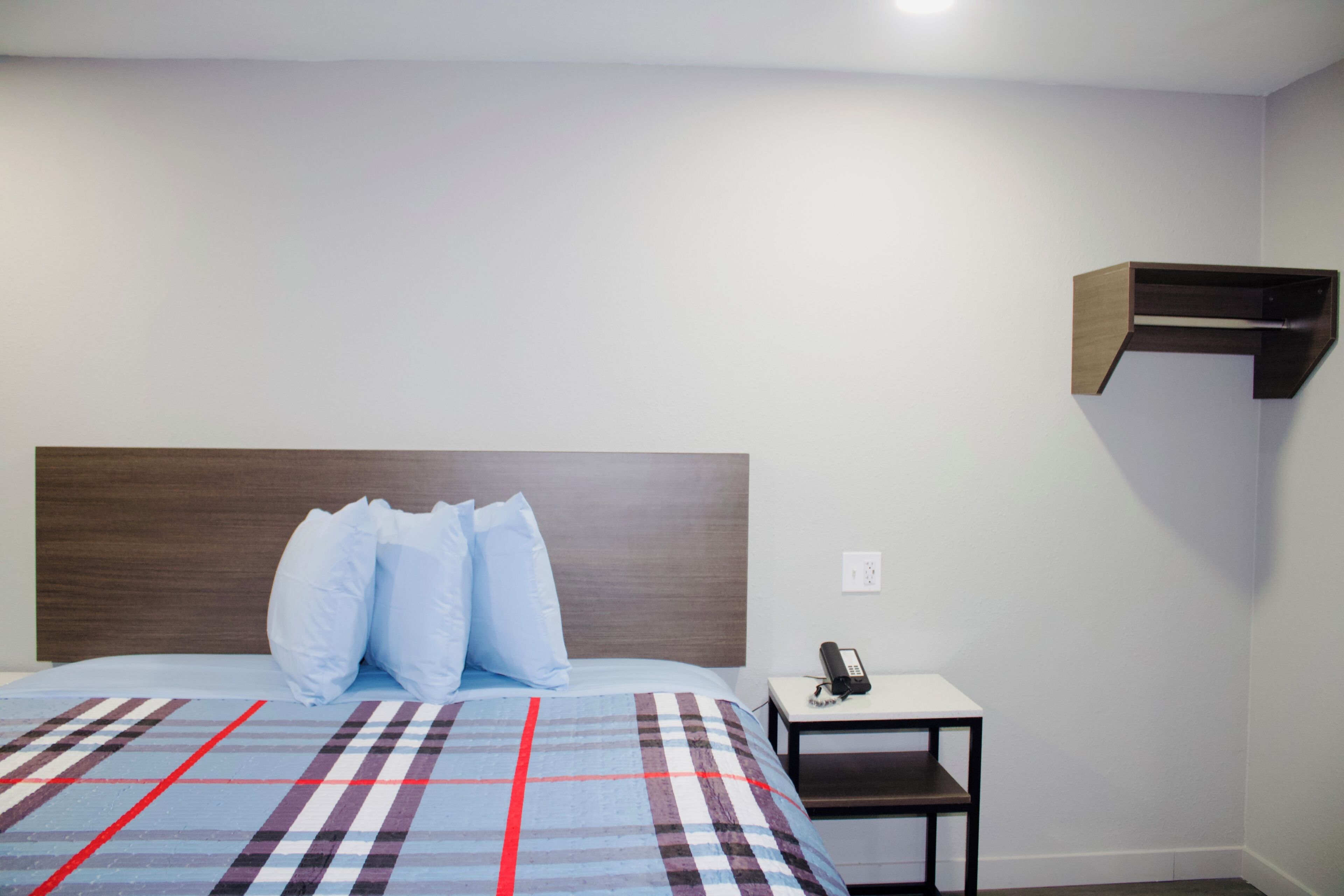 A bedroom with a bed, pillows, a bedside table with a phone, and a wall-mounted shelf.