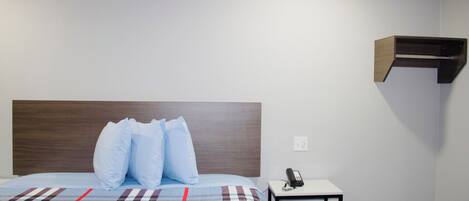 A bedroom with a bed, pillows, a bedside table with a phone, and a wall-mounted shelf.