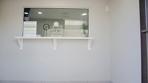 A reception area with a glass window, a white reception desk, a plant, and a welcome mat with 'Homestay Inns & Suites' text. - HomeStay Inn & Suites (Oklahoma City)