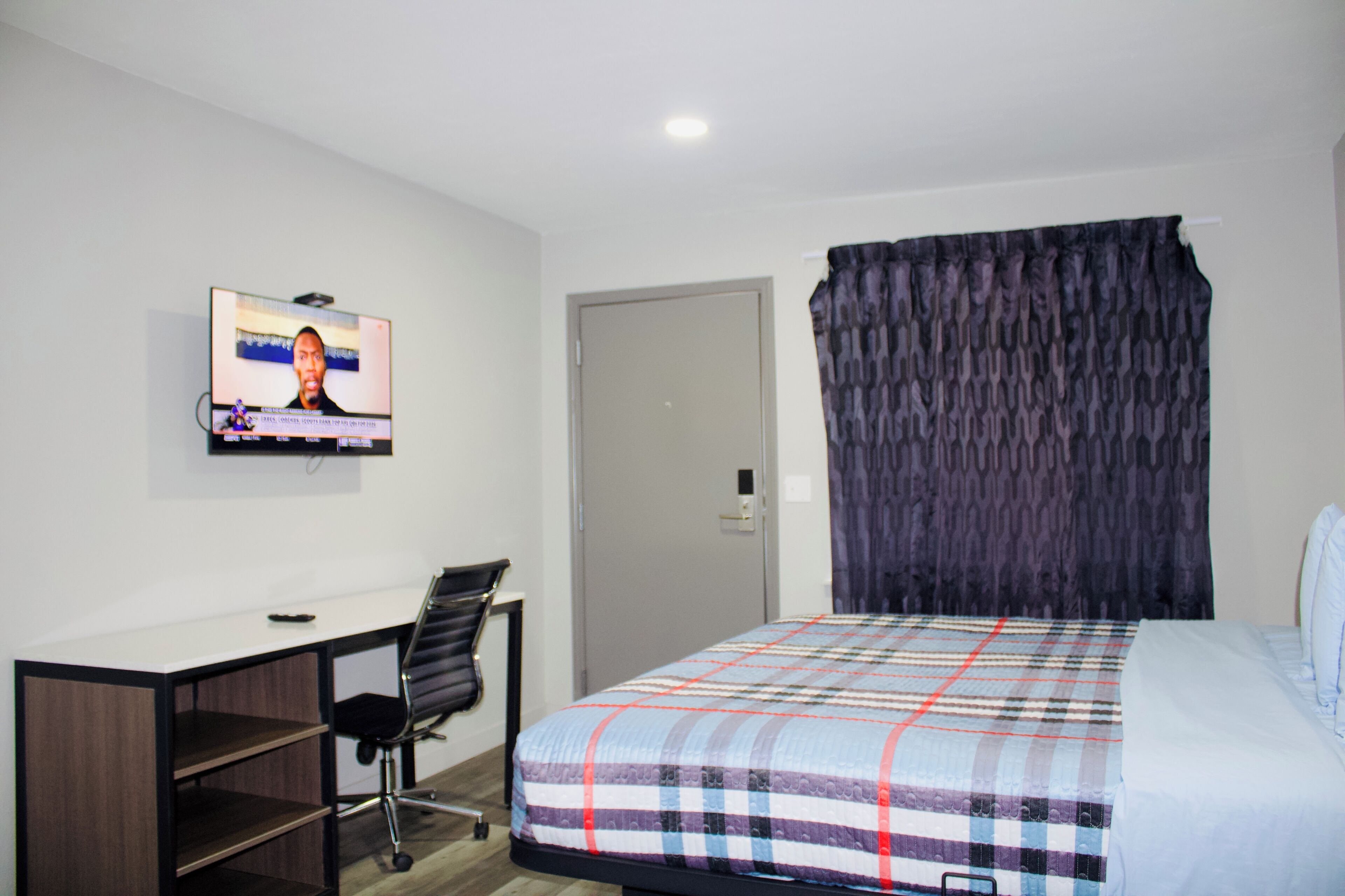 A hotel room with a bed, a desk, a chair, a television on the wall, and a door.