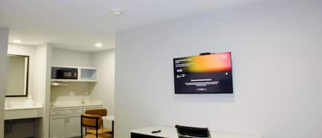 Een hotelkamer met een bed, een bureau, een stoel, een televisietoestel en een kitchenette.