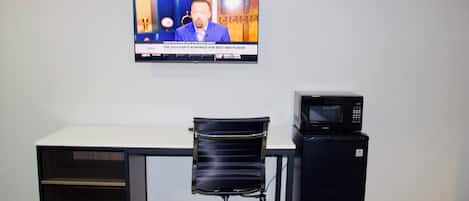 Een kamer met een bed, een bureau, een stoel, een televisie en een magnetron.
