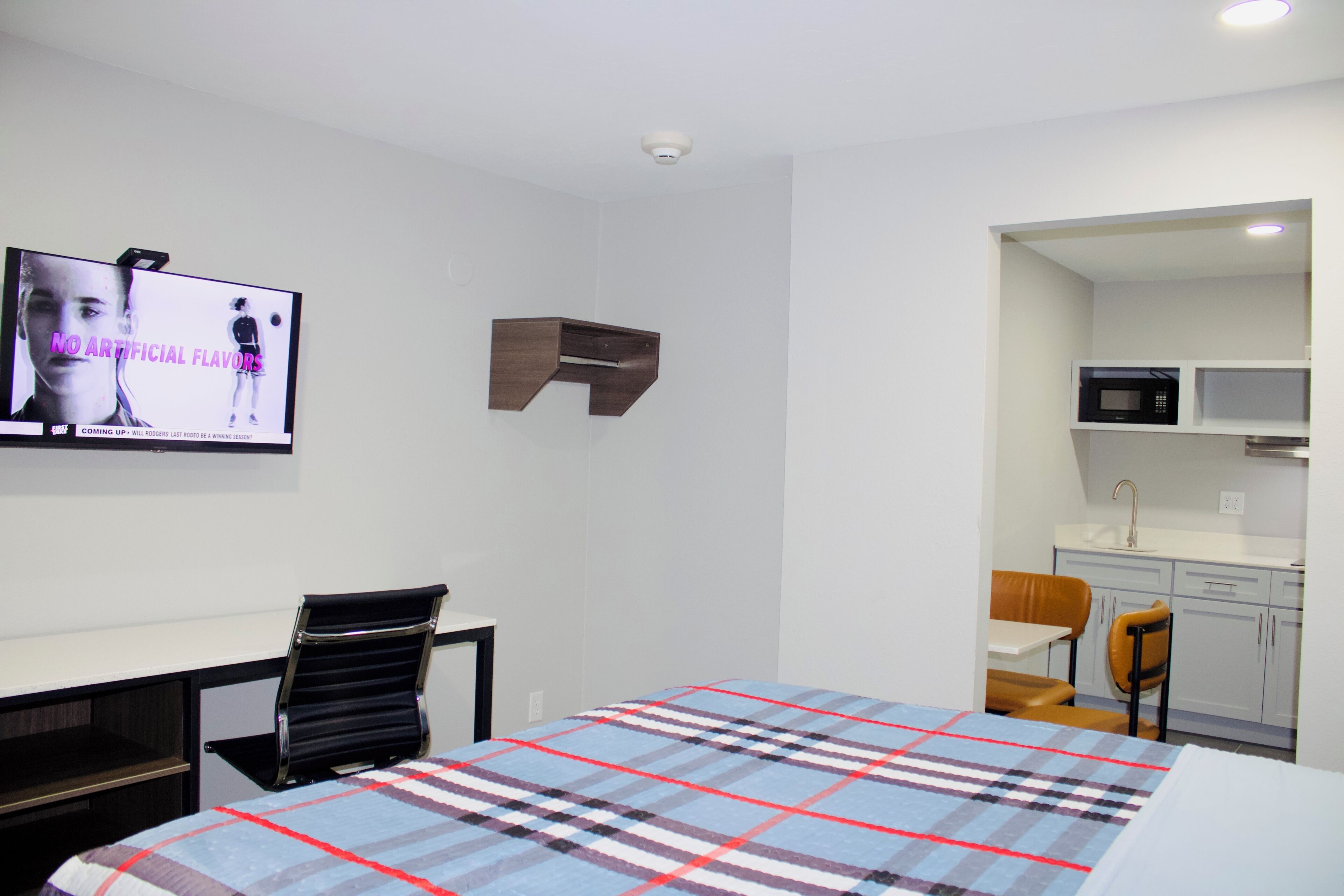 Habitación de hotel con cama, escritorio, silla, televisión, microondas y kitchenette.