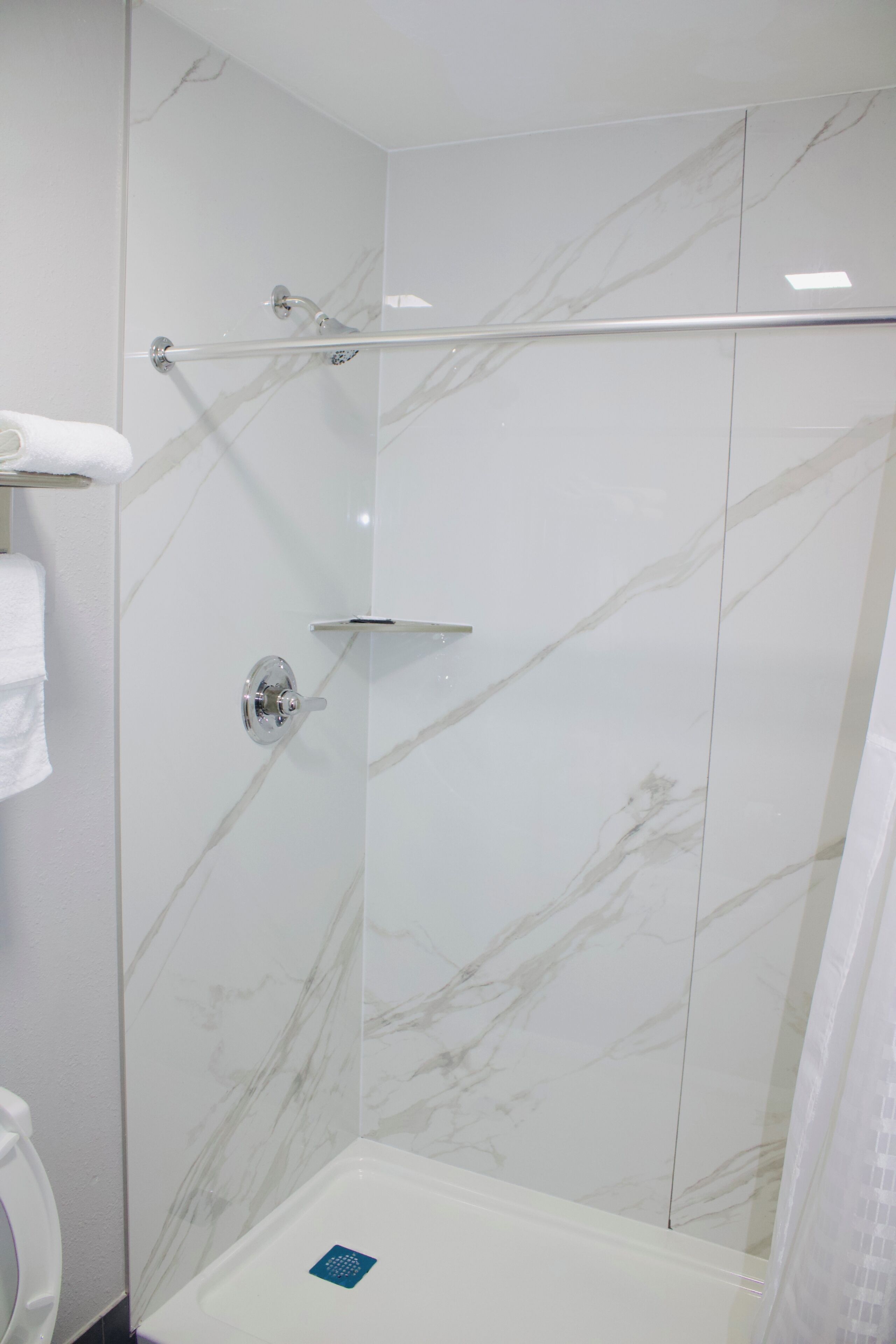 A shower area with a glass door, a handrail, and a white tiled wall with marble-like patterns.