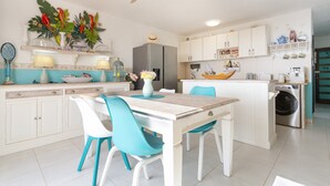 Une cuisine moderne avec des meubles blancs, un îlot central, un ventilateur de plafond et un coin repas avec des chaises.