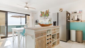 Une cuisine avec un îlot central blanc, un réfrigérateur et un coin repas comprenant une table et des chaises.