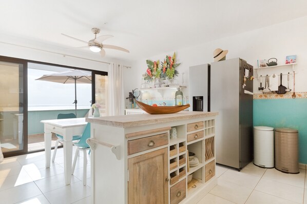 A kitchen with a white island, a refrigerator, and a dining area with a table and chairs.