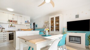 Une cuisine moderne avec des meubles blancs, un îlot central en bois et un téléviseur encastré.