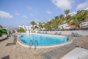 A swimming pool with lounge chairs, palm trees, and a white building in the background.