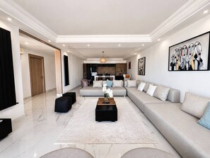 A modern living room with a large sofa, a coffee table, and a dining area in the background. - Marsa Cube House Beachfront Living in La Marsa (La Marsa)
