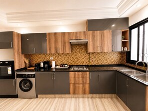 A modern kitchen with dark cabinets, a tiled backsplash, a built-in washer, and a large window. - Marsa Cube House Beachfront Living in La Marsa (La Marsa)