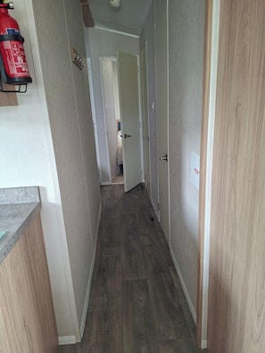 A hallway with wooden flooring, a fire extinguisher mounted on the wall, and a door leading to another room.