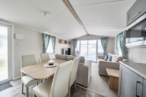 A modern RV interior with a dining area, seating, and a kitchenette.
