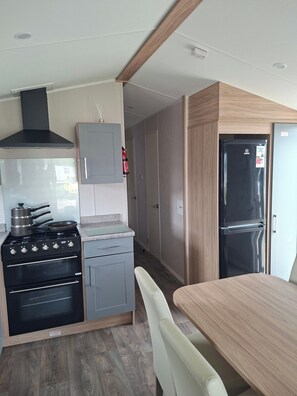 A compact kitchen with a stove, oven, and refrigerator, wooden cabinets, and a dining area with a table and chairs.