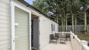 Ein Mobilheim mit Terrasse, Gartenmöbeln und einem umzäunten Hof.